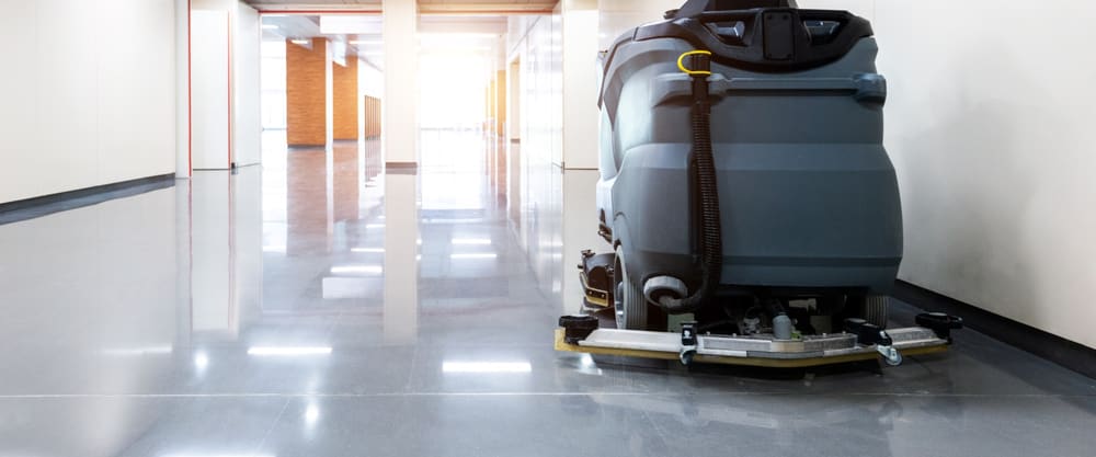 Ride-on floor scrubber parked in a bright corridor with a freshly polished floor